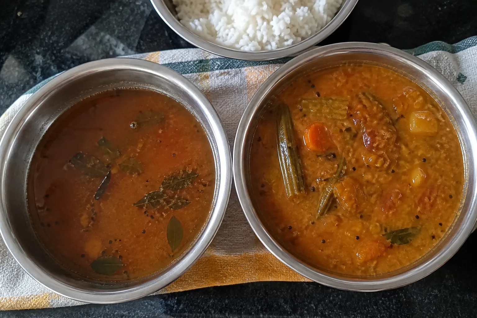 ラッサムとサンバルを並べた比較。手前のラッサムはさらりとした赤茶色、奥のサンバルは豆と野菜で厚みがある