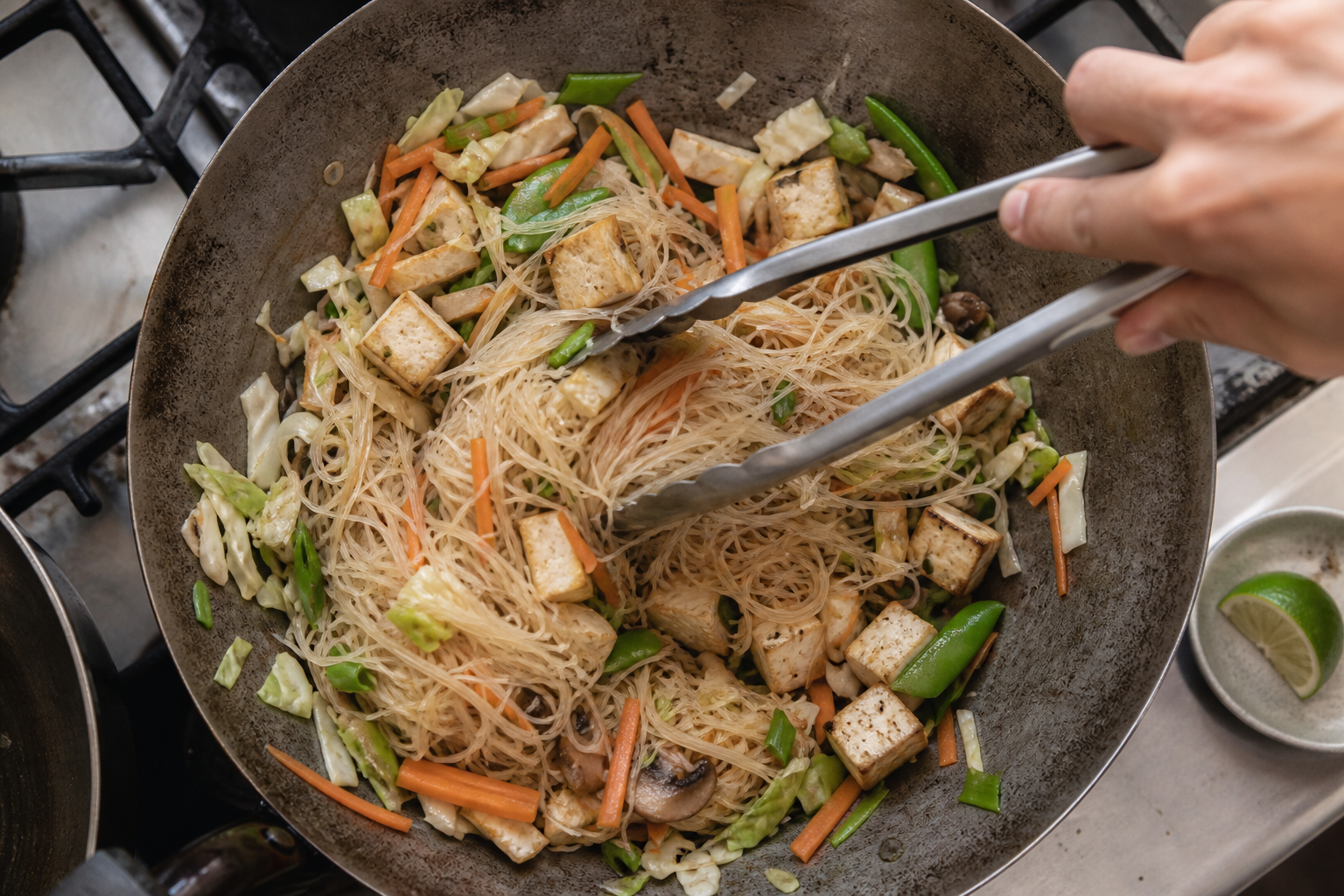 豆腐、きのこ、野菜で作るパンシット・ビーフンの具材を中華鍋で混ぜる様子