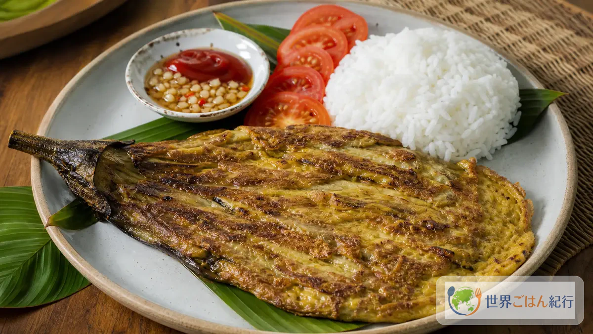 フィリピンの焼きなす卵料理トルタン・タロン。白いご飯、トマト、バナナケチャップ、酢だれを添えた一皿