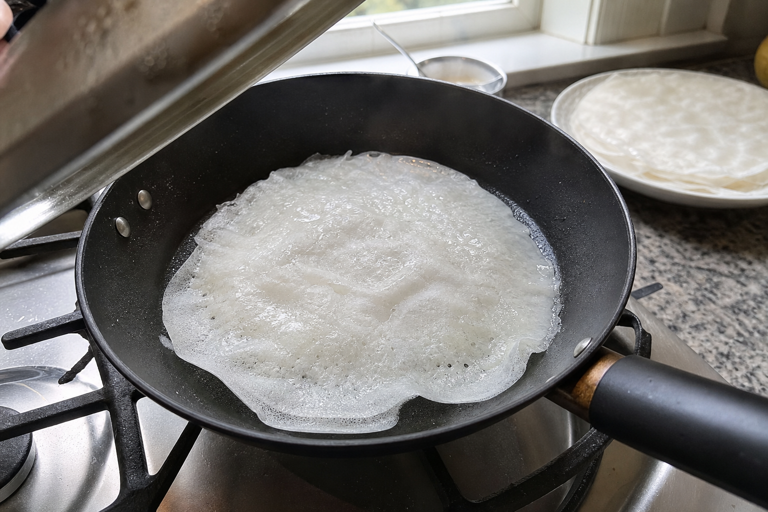 ふたを開けたフライパンの中で半透明になった蒸し米皮。奥に平らな皿と重ねた皮を置いている
